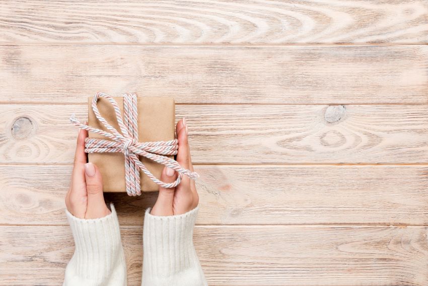 Caja de regalo navideña con un lazo elegante, sobre un fondo festivo con adornos.
