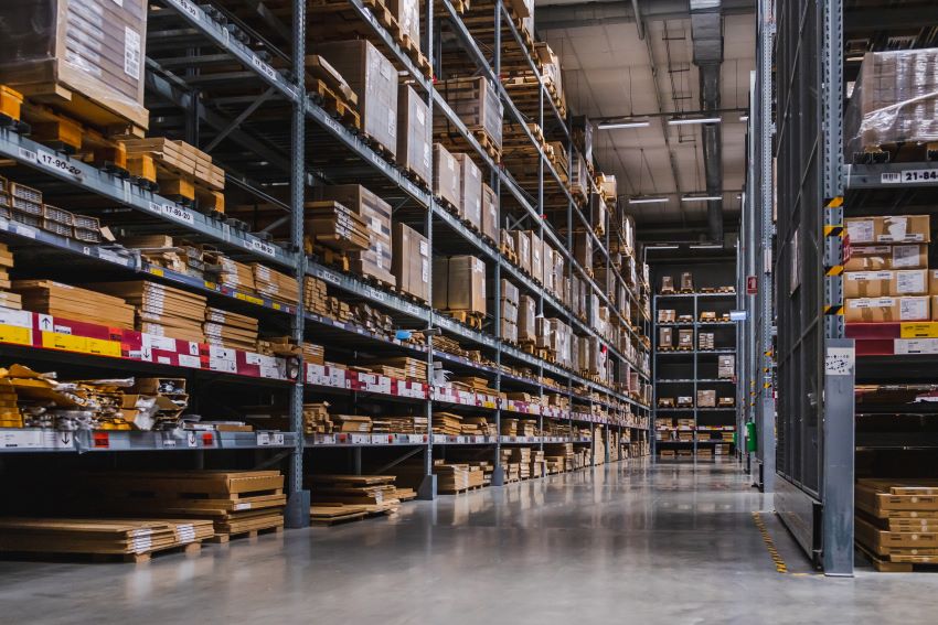 Hombre trabajando en un almacén organizado con cajas en estantes y pasillos amplios, enfocado en optimización logística de